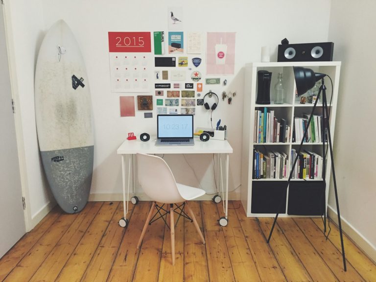White surfboard beside white wall white wooden cube bookshelf inside the room